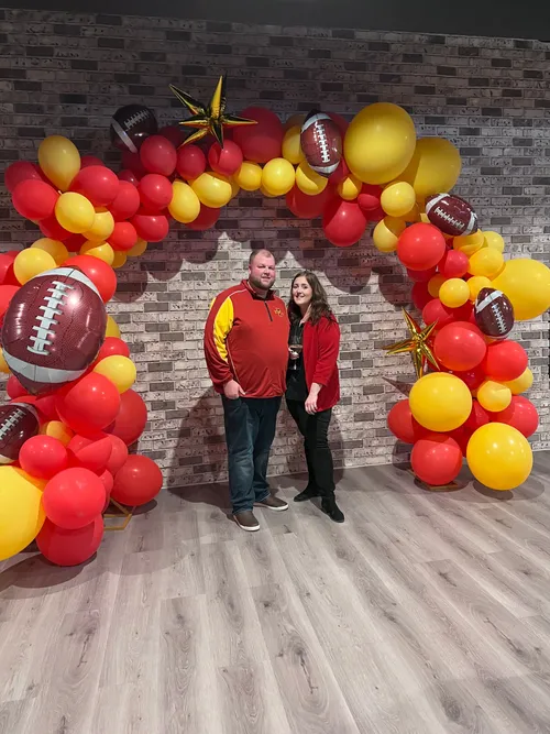 football themed red and yellow balloon arch with couple standing under it