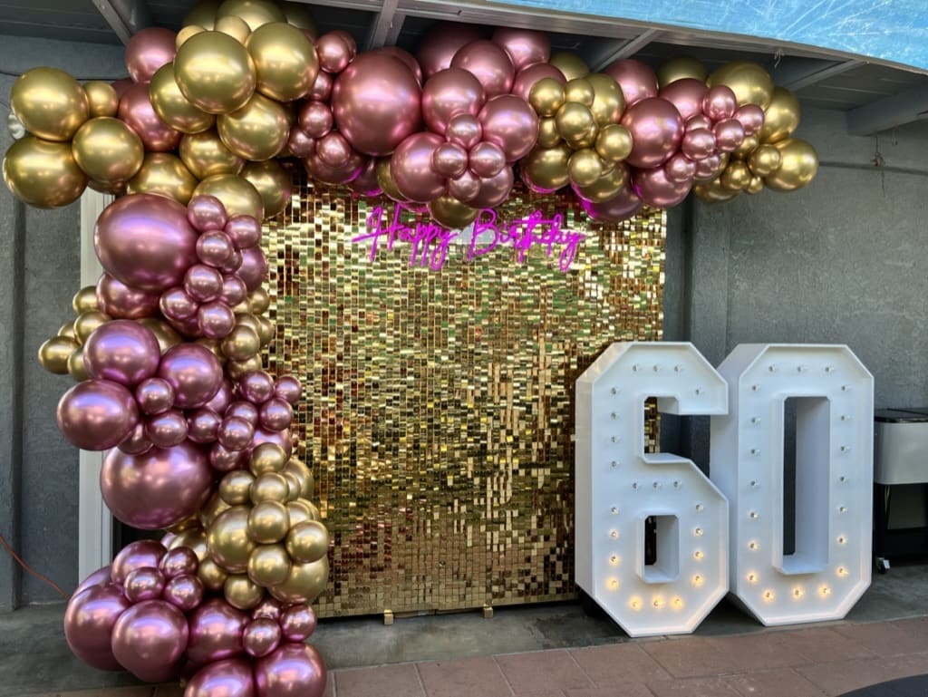 60th birthday balloon decor installation with light up marquee and pink and gold balloon garland