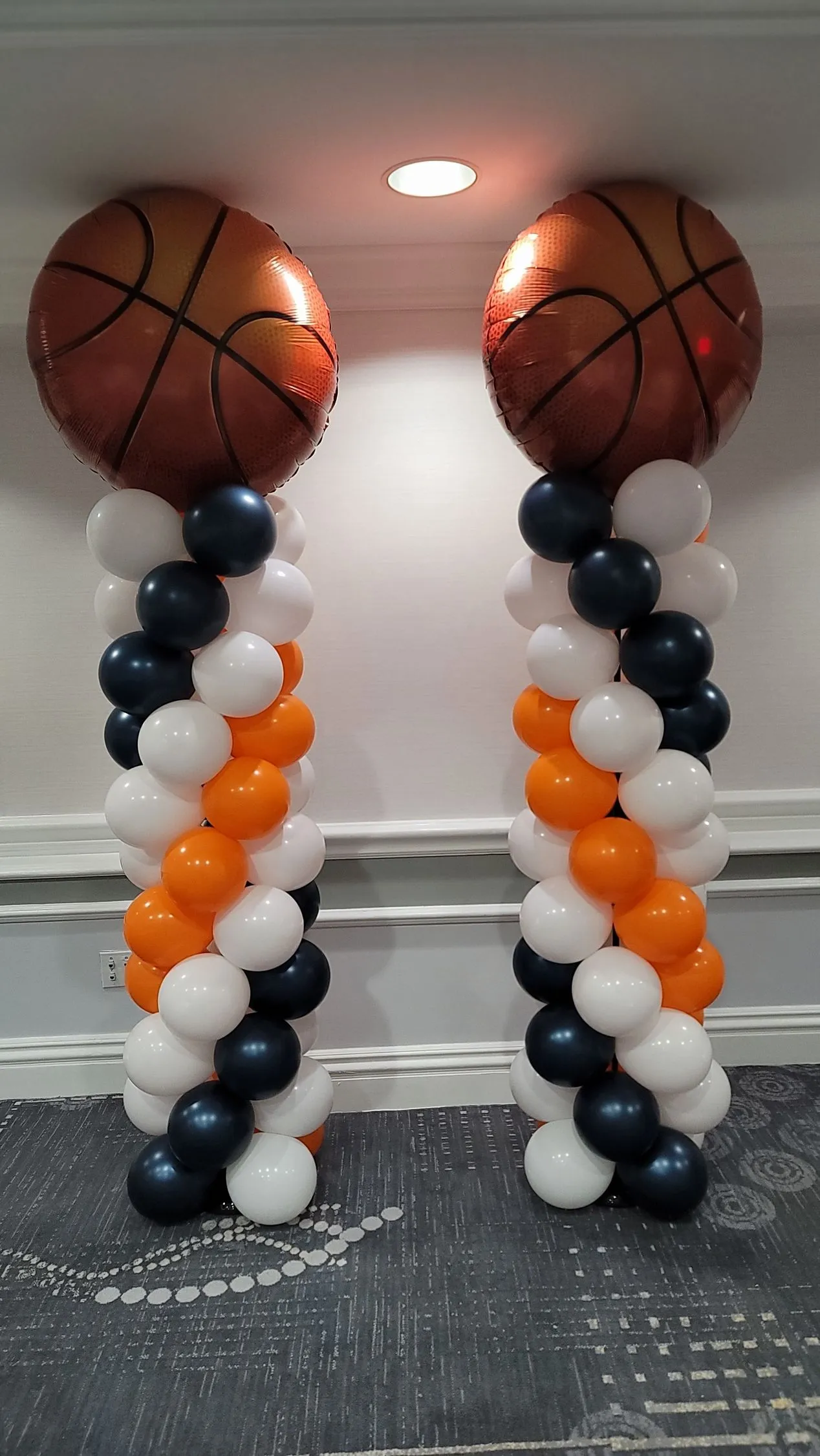 two large orange, black, and white basketball themed balloon columns