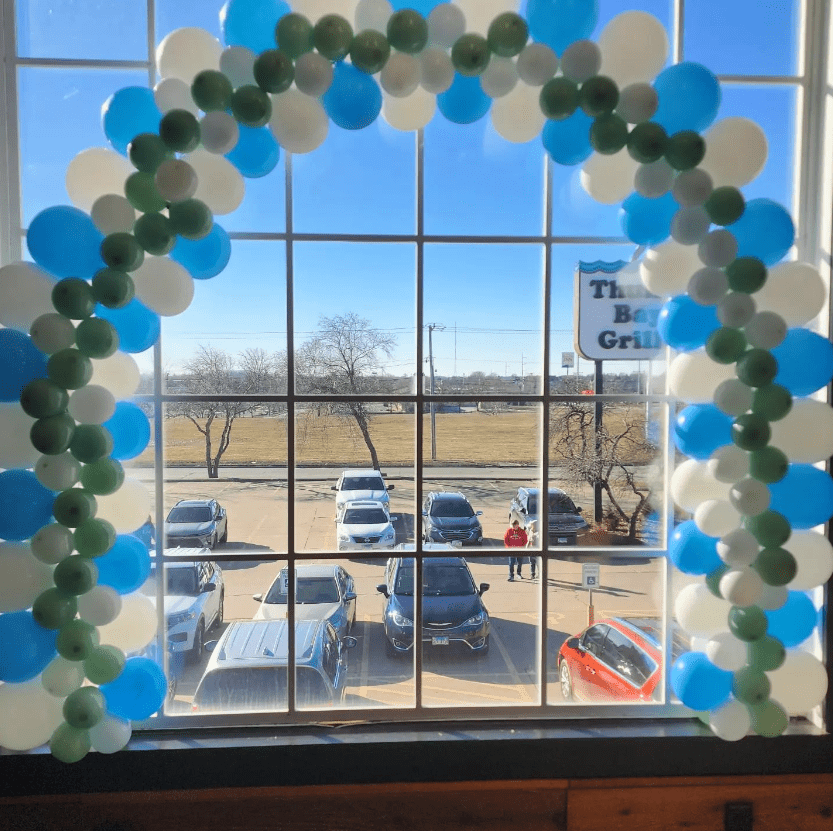 large blue, white, and green balloon arch in front of window