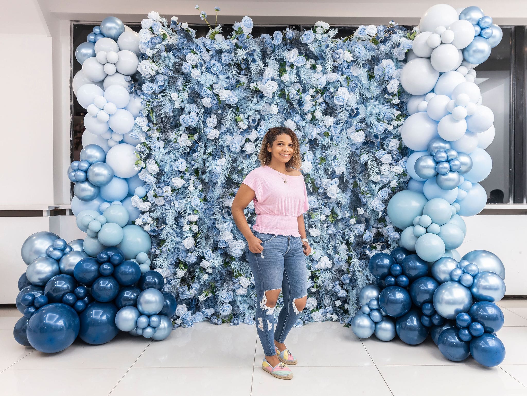 young woman standing in front of a blue and white balloon wall