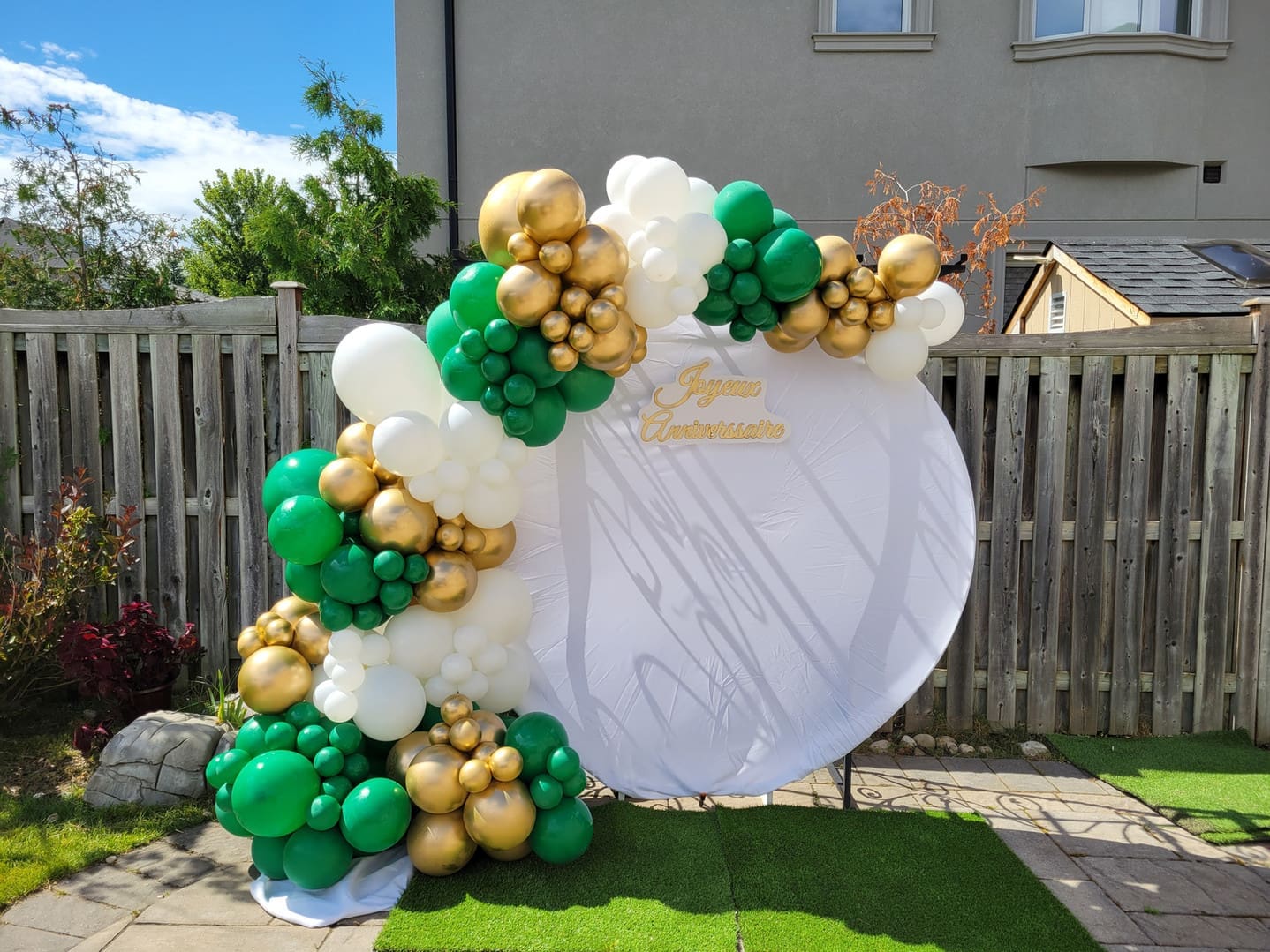 an anniversary balloon garland backdrop that is green, gold, and white